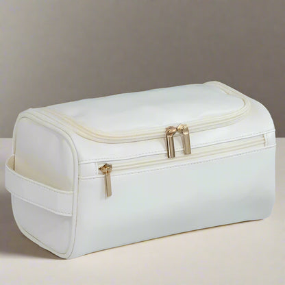 White toiletry bag with gold zippers on a light gray background