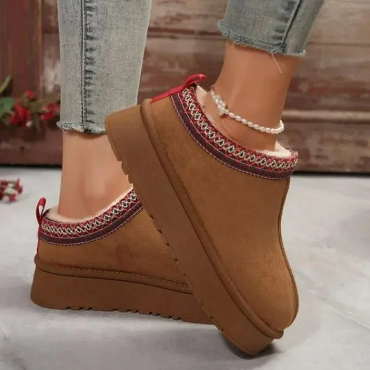 Brown slip-on shoes with decorative trim worn indoors on a light wooden floor.
